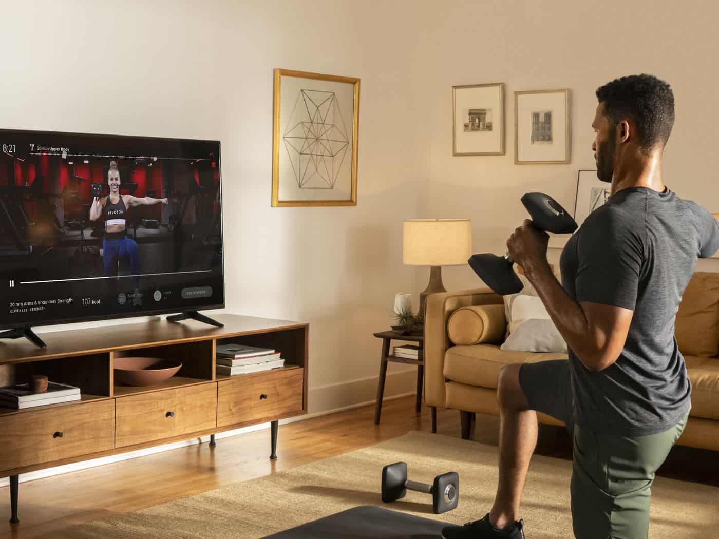 Man working out with dumbells using Peloton App on TV