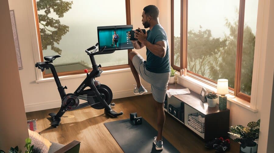 Man exercising with dumbells next to a Peloton Bike